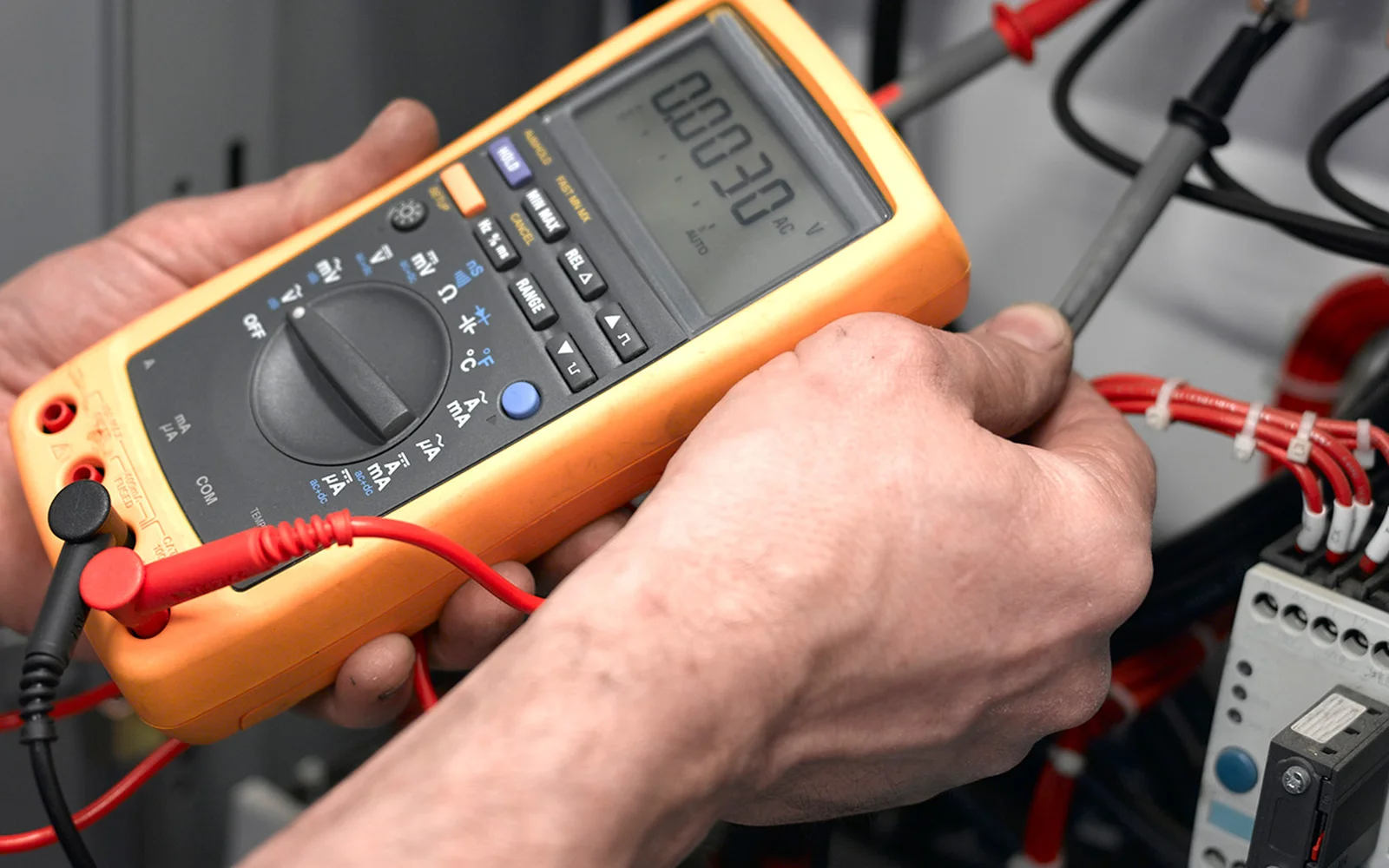 Close-up of a multimeter probe testing a contactor terminal during a diagnostic check